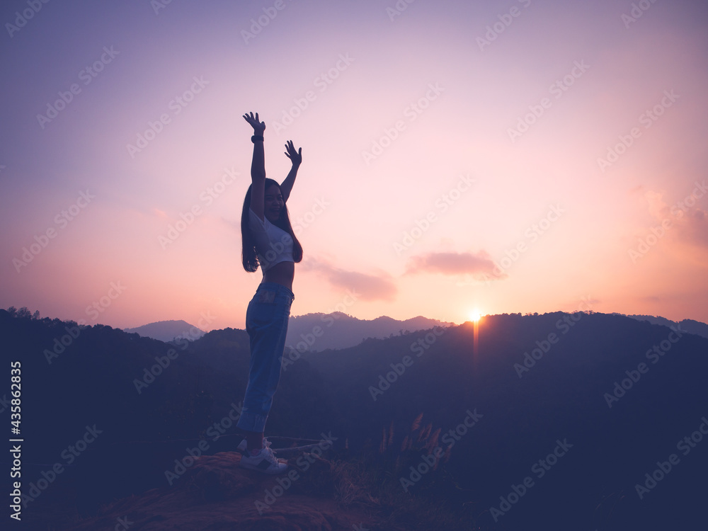 Silhouette of woman enjoying the sunset with dramatic sky on mountain peak.