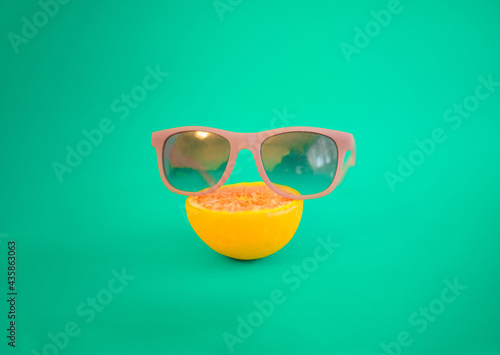 Sunglasses and orange on a blue-green background. Pastel and neon colors are in trend. Minimalist depiction of the summer period.