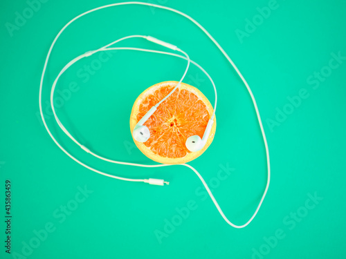 It's party time. Orange fruit with headphones . Blue-green background and pastel colors. Party is comming. Citrus fruits.