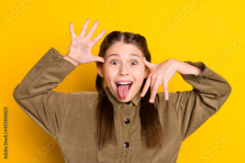 Photo portrait of small playful childish girl grimacing fooling showing tongue isolated on bright yellow color background