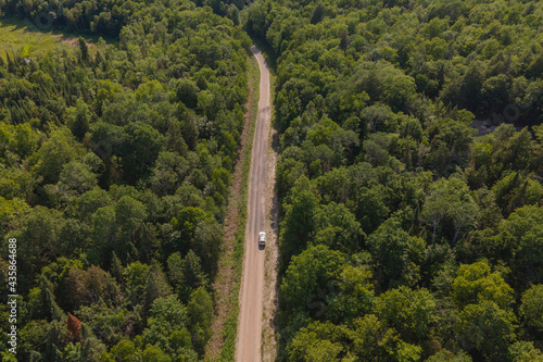 Aerial bird's eye view drone panorama of green coniferous forest, fresh water lakes and rivers and car driving on unpaved road winding trough the trees. Summer sunny day, blue sky.