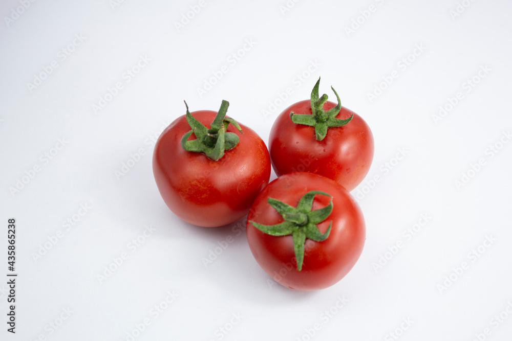 Three fresh red tomatoes with green leaves on white background. Three fresh red tomatoes with green leaves on white background.