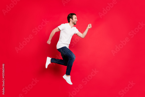Full size profile photo of young brown hairdo man run wear white t-shirt jeans isolated on red color background