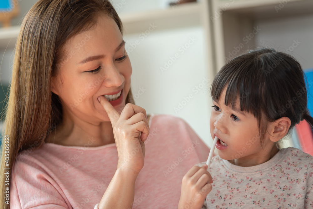 Asian child brushing teeth with mother in bathroom