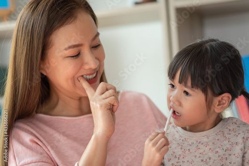 Asian child brushing teeth with mother in bathroom