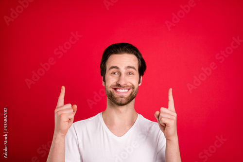Photo of cheerful happy young man point fingers up empty space good mood isolated on red color background