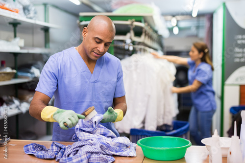 Portrait of dry cleaning employee at work, man cleaning shirt with brush