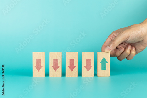 Hand holding wooden cube green with arrow pointing up facing the opposite direction red arrows down. Concept of different thinking idea