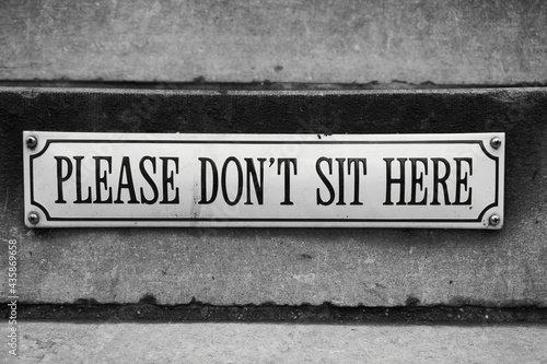 A sign on a building requesting from people to not sit here.