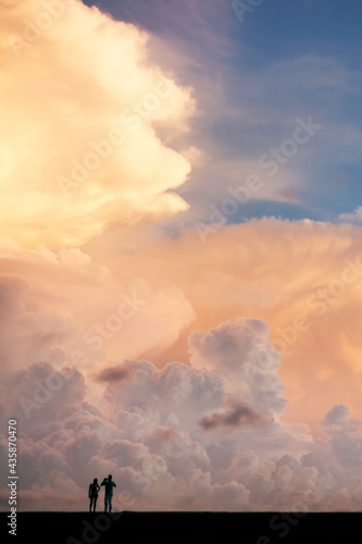 The silhouette of two boys taking a picture under a sky of colored clouds