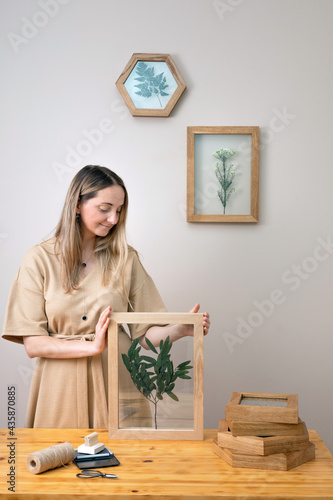 woman decorates Dry flowers in a frame. walls with botanical leaves. Eco-friendly boho decor. Real people personal space.  © alas_spb