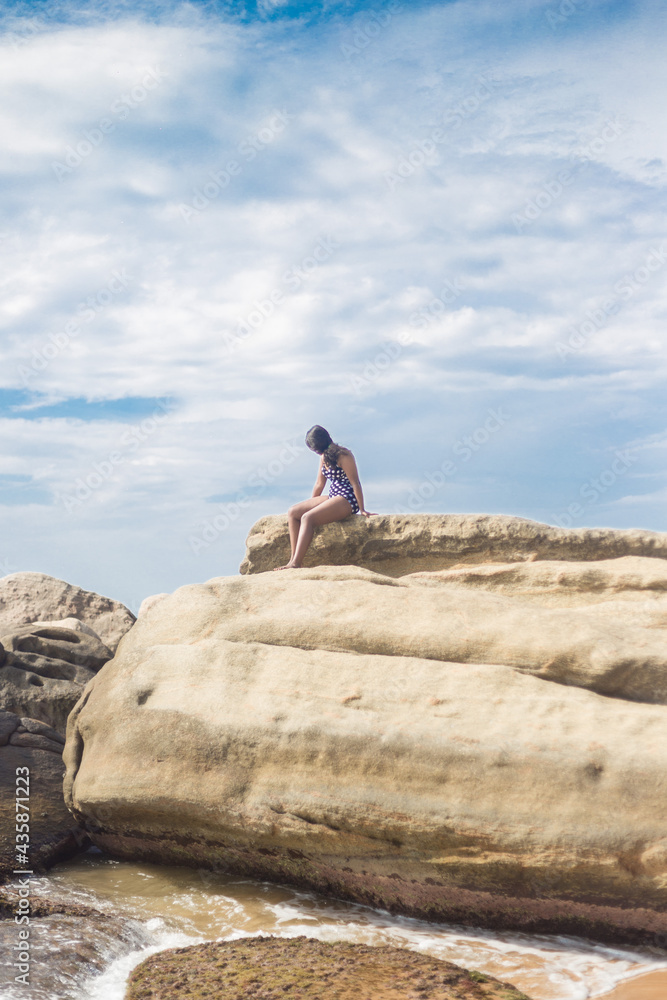 A girl sitting on a rock near the beach