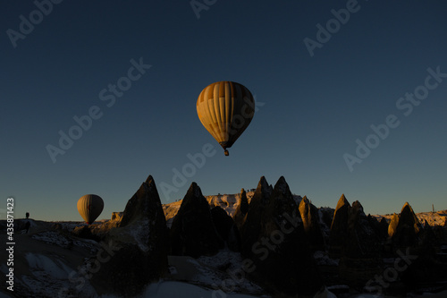 Two huge colourful hot air balloons ascending at sunrise flying over the valleys and the rock formations of Goreme in Cappadocia, Anatolia, Turkey