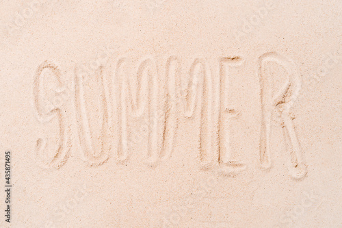 the word summer written with the finger on a sandy beach background. concept of summer and holidays. copy space.