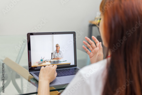 Asian female patient having online video call with doctor on laptop. Young woman talking to medical practitioner consulting health specialist over internet. Online medical consultation concept.