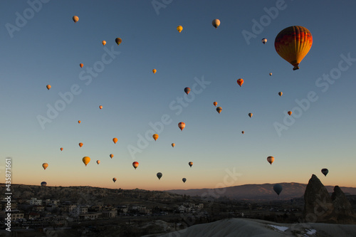 Tens of colourful hot air balloons flying over the valleys and the city of Goreme in Cappadocia, Anatolia, Turkey in the light of sunrise