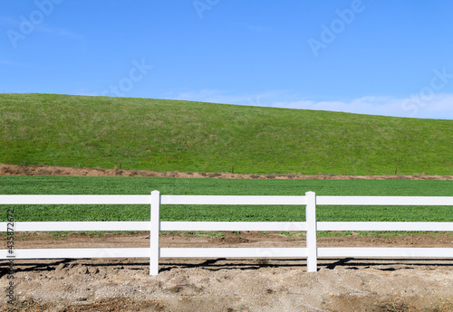 low grassland hillside hills pasture with bright sunny blue sky and wooden white picket farm livestock fence
