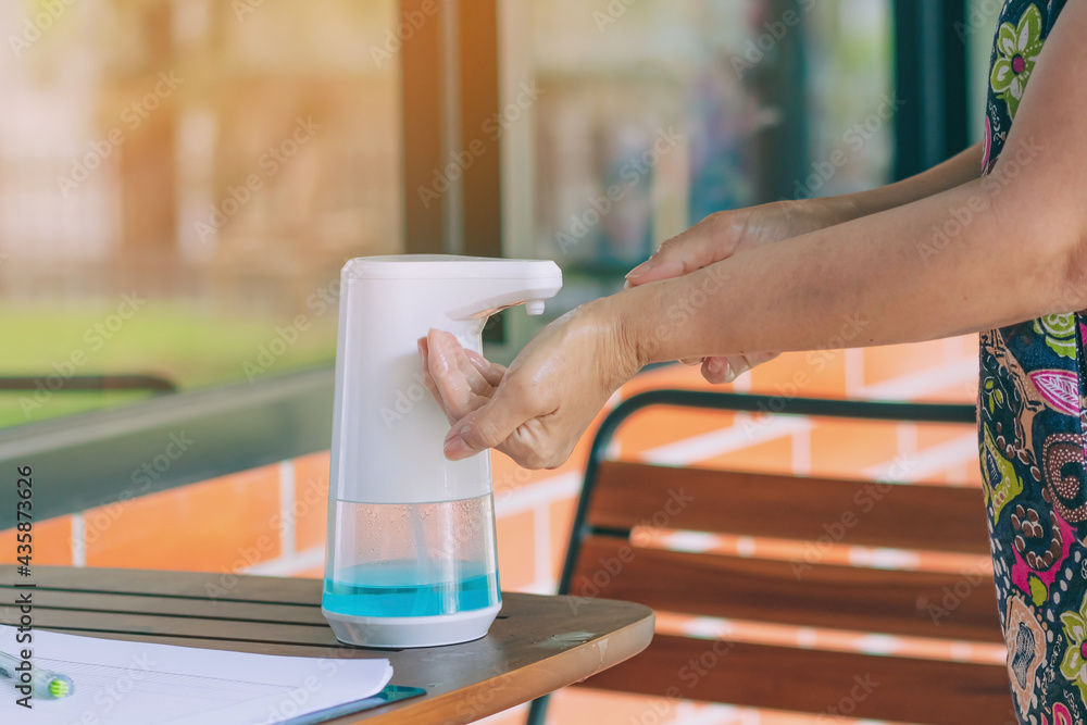 Obraz premium Automatic alcohol dispenser for cleaning hand to prevent the spreading of Coronavirus (Covid-19) on table before entrance to cafeteria. Healthcare concept. New normal lifestyle. Selective focus