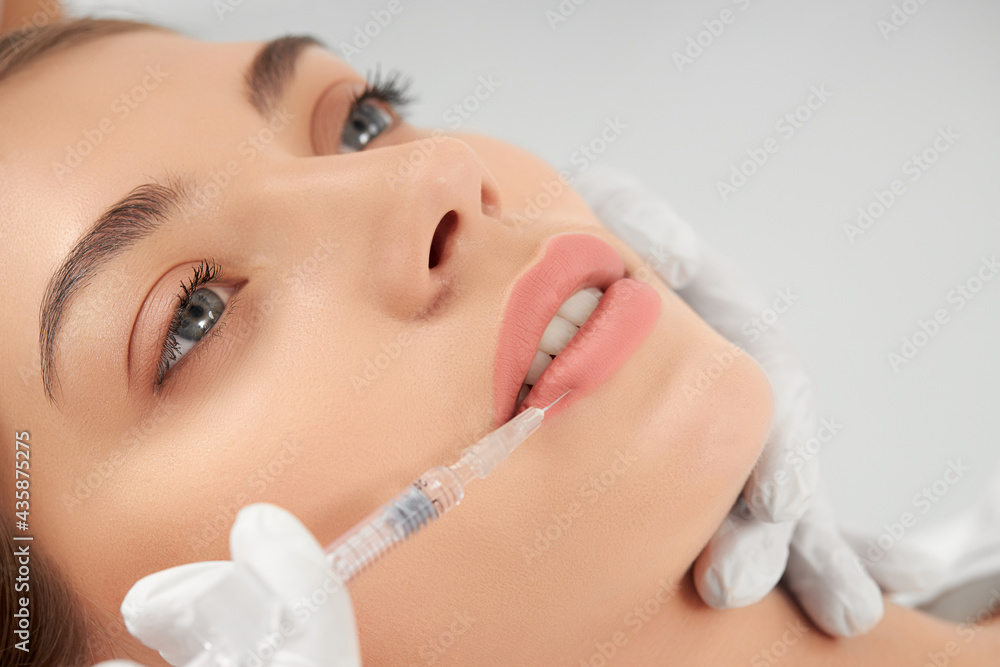 Close up portrait of attractive young woman on procedure injection in lip with special preparation. Concept of process procedure lip augmentation in professional salon.