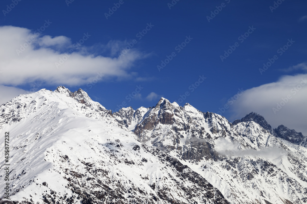 High snowy winter mountains and blue sky with clouds at sun day