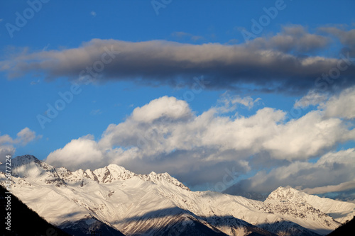 High snowy winter mountains in sunlight clouds at sunny evening © BSANI