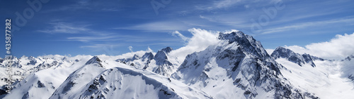 Panorama of high snow-capped mountain peaks and beautiful blue sky with clouds