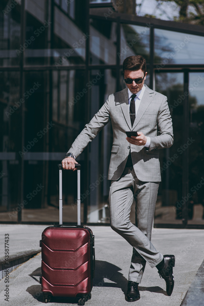 Full length happy young employee business man in grey suit stand near  office glass wall building