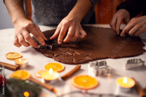 Mother and her little son cutting dough in different forms to bake christmas cookies, burning candles and other decorations on the foreground