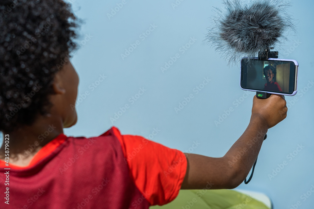 Portrait of smiling African-American boy waving at camera while holding  selfie stick and video blogging from home, copy space Stock Photo | Adobe  Stock