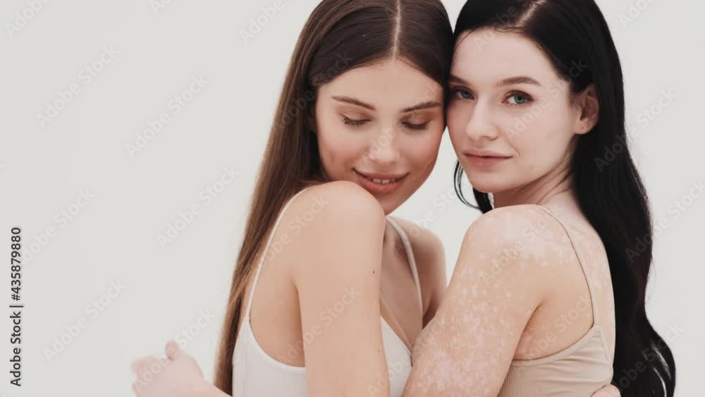 The two girls in knitted tops hugging each other while standing in a white studio The two girls in knitted tops hugging each other while standing in a white studio