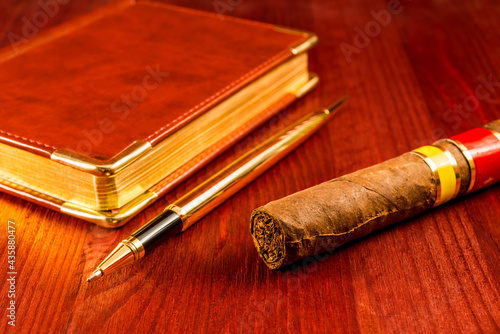 Golden pen with a leather diary and cuban cigar on a mahogany table