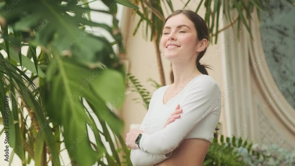 The side view of a positive woman looking at the green flowers while standing with crossing arms in the garden The side view of a positive woman looking at the green flowers while standing with crossing arms in the garden