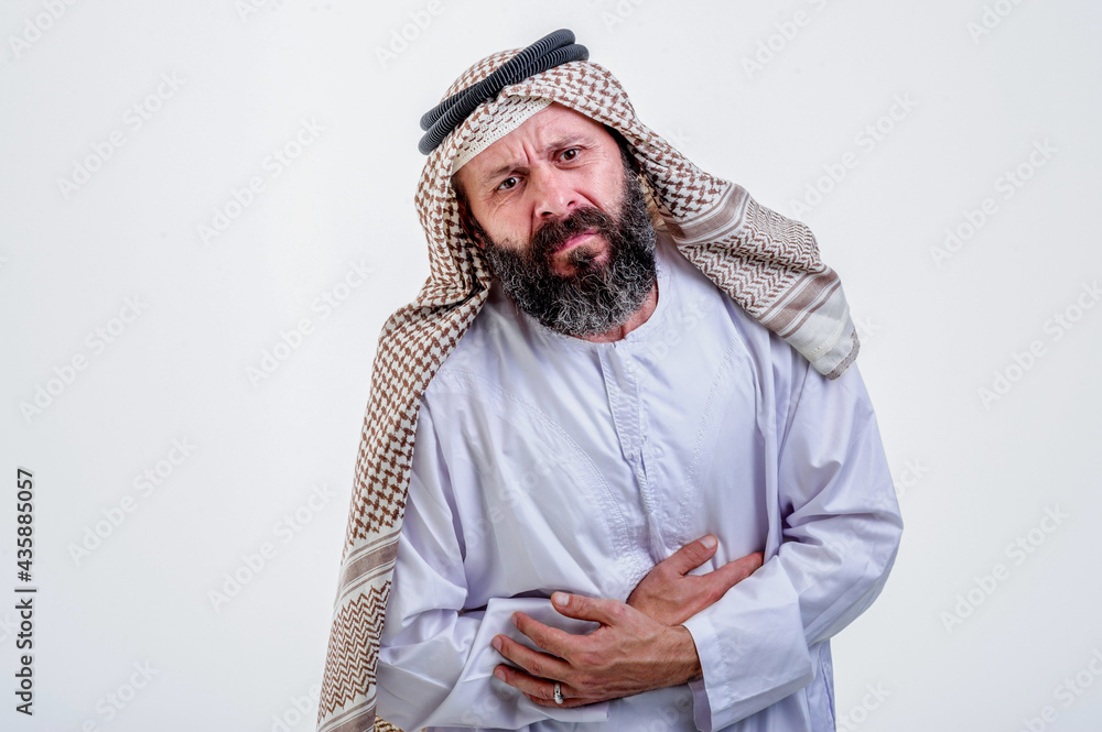 Portrait of young muslim Arabic man squezze his stomach for having stomachache pain, against white background