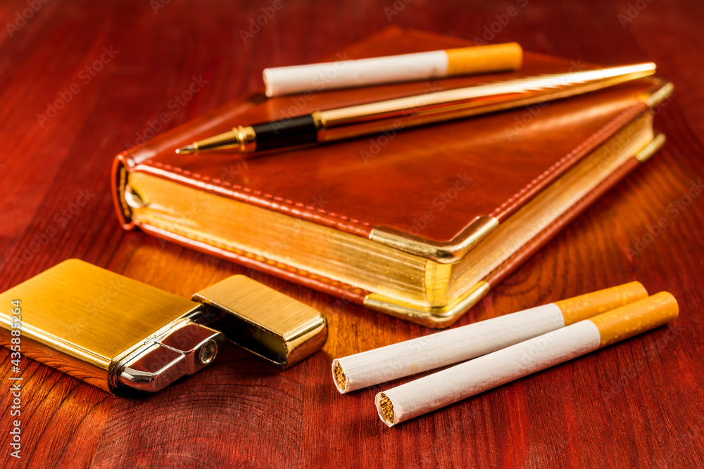 Leather diary and cigarettes with open golden lighter and pen on a mahogany table Leather diary and cigarettes with open golden lighter and pen on a mahogany table