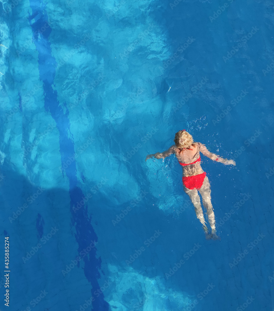 Girl swimming in the pool, in a red swimsuit, with a beautiful figure, in clear blue water.
