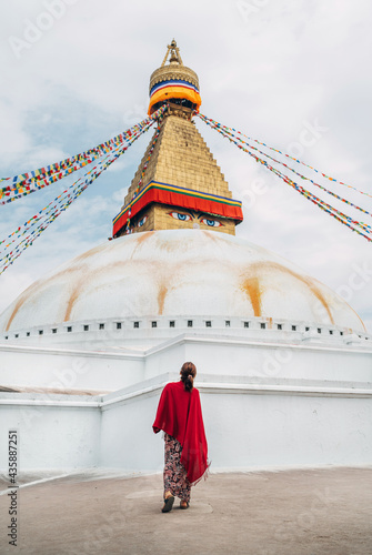 Canvas Print Female dressed long summer dress with red shawl walking by square near Boudhanath Stupa - the largest spherical stupas in Nepal