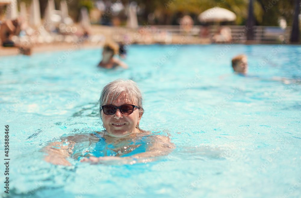 Elderly senior woman with grey hair, wearing blue swimsuit smiling in hotel pool