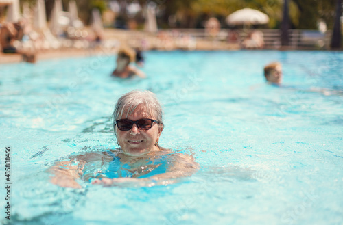 Elderly senior woman with grey hair, wearing blue swimsuit smiling in hotel pool