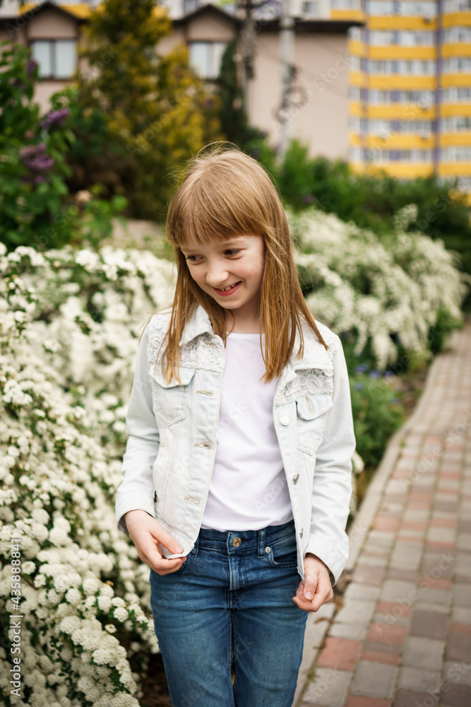 Obraz premium smiling girl in a white denim jacket near a flowering white bush