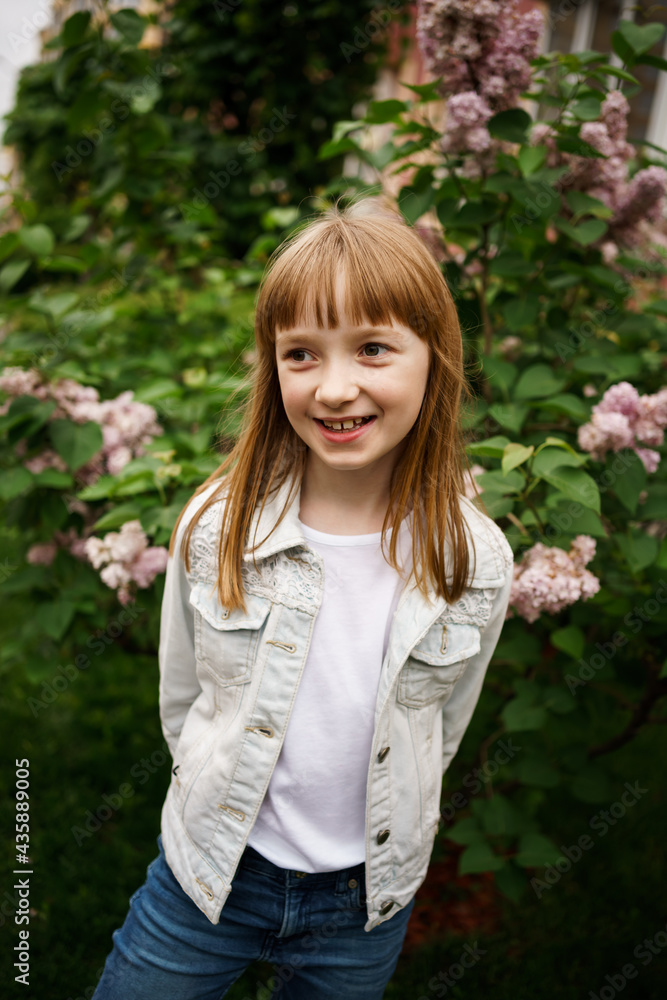 smiling girl in a white denim jacket near a bush of blooming lilacs smiling girl in a white denim jacket near a bush of blooming lilacs