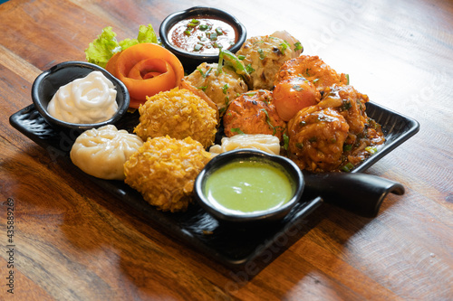 tandoori fried roasted momos dimsum pakora with vegetable flower chicken and green, white and red sauce put in a black plate on a wood table