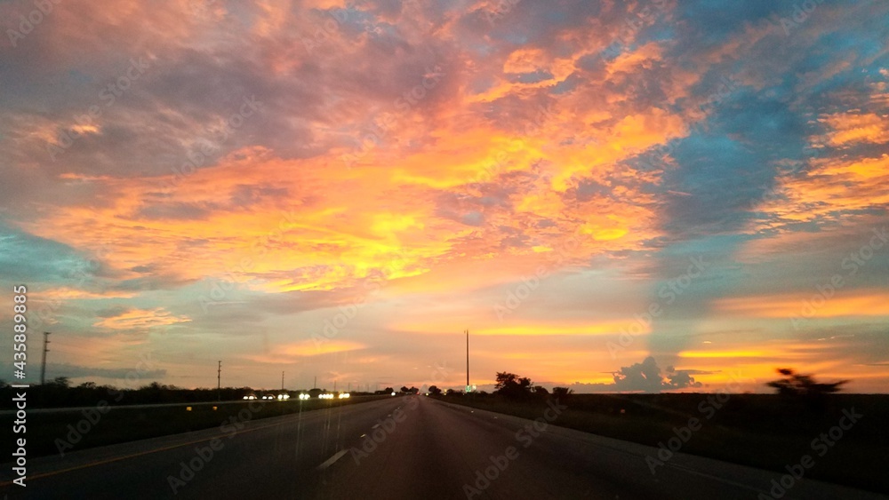 Pink and yellow clouds over a highway at sunset