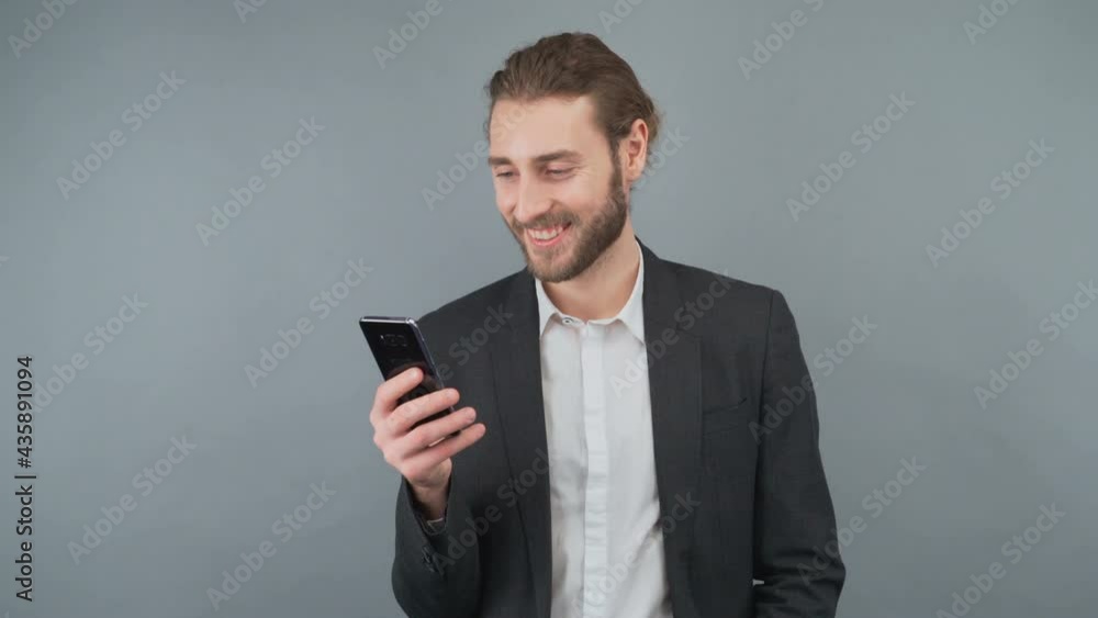 Male businessman in a gray suit browsing pages on a smartphone. A man touches the smartphone screen. Man on isolated gray background in studio. Male businessman in a gray suit browsing pages on a smartphone. A man touches the smartphone screen. Man on isolated gray background in studio.