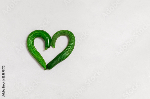 Top view of bent ugly cucumbers in heart shape on grey concrete background with copy space