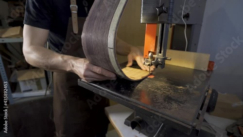 Anonymous luthier cutting guitar body on bandsaw in workroom photo