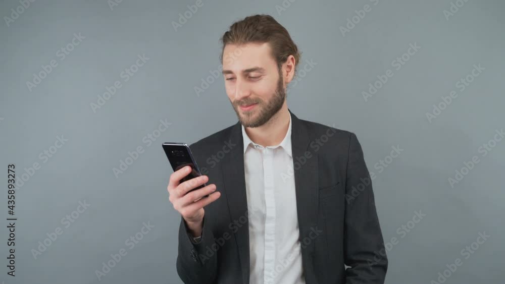 Male businessman in a gray suit browsing pages on a smartphone. A man touches the smartphone screen. Man on isolated gray background in studio. Male businessman in a gray suit browsing pages on a smartphone. A man touches the smartphone screen. Man on isolated gray background in studio.
