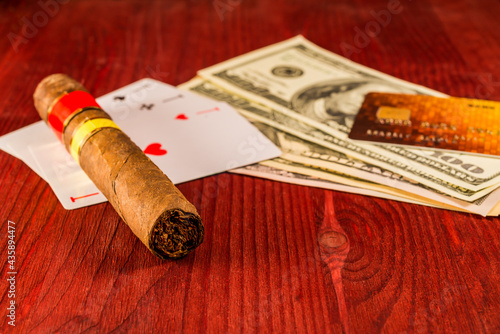 Cuban cigar with playing cards and money with payment card on the table mahogany. Focus on the cuban cigar, identification cards ace Russian letter