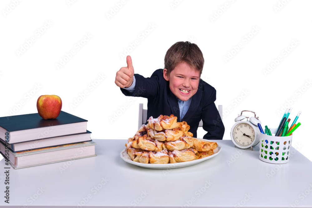 Unhealthy and wholesome food of schoolchildren in elementary school, isolated on a white background. Boy at a school desk with a plate of sweets Unhealthy and wholesome food of schoolchildren in elementary school, isolated on a white background. Boy at a school desk with a plate of sweets