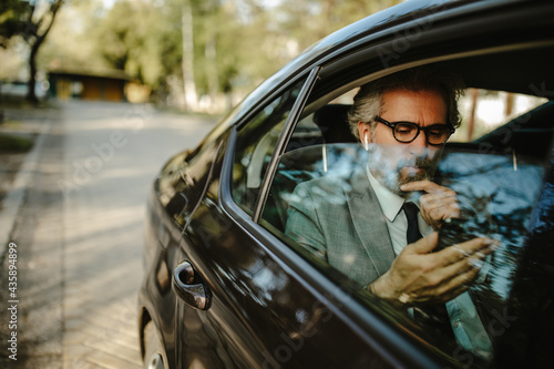 Happy middle aged businessman using cell phone, having video call and using wireless earphones.