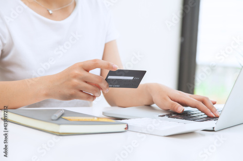 A woman sits in the house with a laptop and holds a credit card to shop online. The concept of online shopping